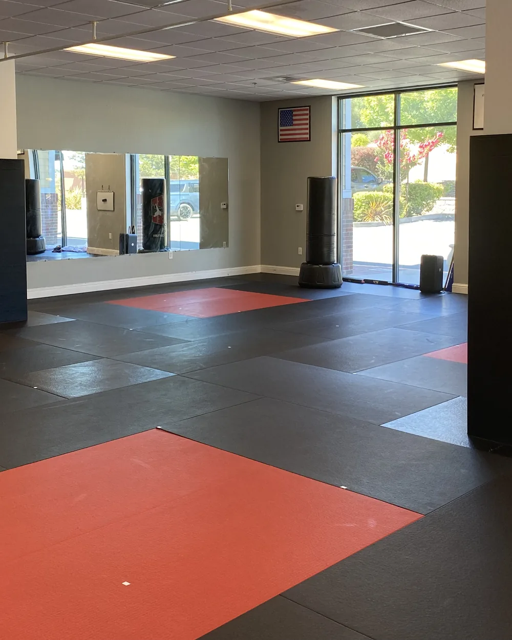 The training floor at Element ATA Martial Arts in Martinez CA, with red and black mats, wall mirrors, and heavy bags along the windows