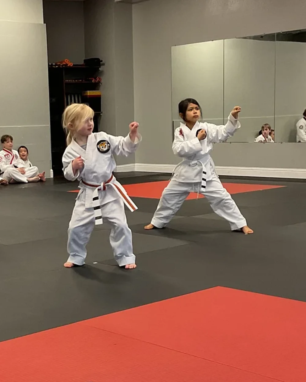 Two young ATA Tigers students holding a Taekwondo form stance with fists raised while classmates watch from the edge of the mat at Element ATA Martial Arts in Martinez CA
